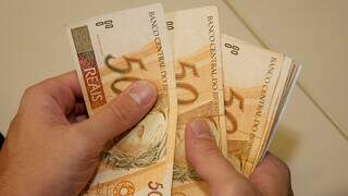 Homem conta cédulas de dinheiro; média salarial é maior para homens, no Brasil. (Foto: Arquivo/Campo Grande News)