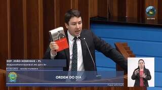 Deputado estadual João Henrique Catan (PL) segurando livro que conta a história de Adolf Hitler na tribuna da Assembleia Legislativa, na última terça-feira (7). (Foto: Reprodução)