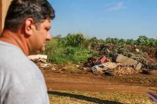 Rayan olha terreno baldio com lixo, sofá e pneus jogados, próximo a sua casa, no bairro Caiobá (Foto: Henrique Kawaminami)