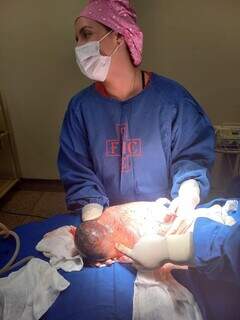 Médica segura o bebê ainda empelicado após o parto (Foto: MS Todo Dia)