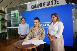 Prefeita de Campo Grande assinando convênio de turismo com Sebra-MS, ao lado da secretária de Cultura, Mara Bethânea Gurgel. (Foto: Roberto Ajala)