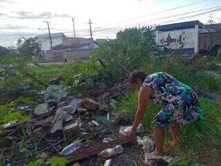 Graciela tirando água de garrafas jogadas em terreno do centro comunitário. (Foto: Mylena Fraiha)