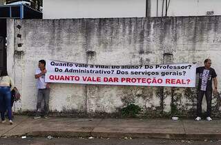 Guardas municipais seguram cartaz da campanha em frente à Escola Municipal Bernardo Franco Baís, na manhã desta segunda-feira (22). (Foto:Divulgação/SindGM/CG)