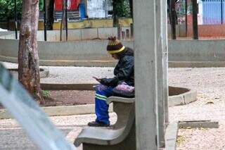 De touca e casaco, mulher observa o celular em praça de Corumbá (Foto: Juliano Almeida)