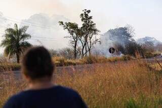 Moradora observa fumaça do outro lado da rodovia (Foto: Henrique Kawaminami)