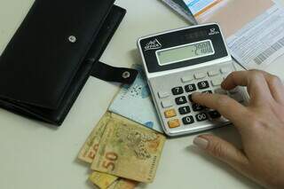 Mulher faz conta na calculadora e contabiliza dinheiro (Foto: Arquivo/Campo Grande News)