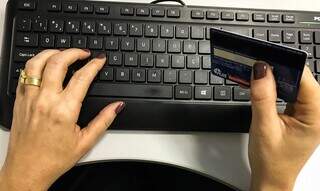 Mulher segurando cartão enquanto mexe em computador (Foto: Marcello Casal Jr./Agência Brasil)