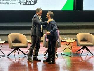 Governador Eduardo Riedel e deputado Pedro Kemp no palco durante lançamento de benefício social (Foto: Lucimar Couto) 