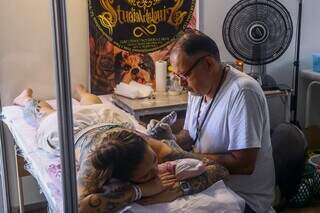 Em um dos stands do evento, tatuador realiza sessão com uma cliente. (Foto: Paulo Francis)