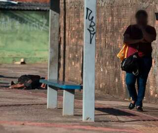 Mulher espera ônibus na Vila Nhanhá, enquanto dependente químico dorme ao fundo. (Foto: Marcos Maluf)