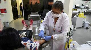 Funcionária do Hemosul retirando bolsa de sangue de doadora (Foto: Bruno Rezende/Governo do Estado)