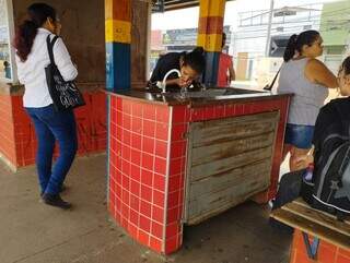 Usuária do transporte público bebe água quente no Terminal Morenão, em Campo Grande (Foto: Alison Silva)