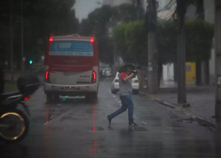 Homem atravessa avenida tentando se proteger da chuva. (Foto: Henrique Kawaminami)