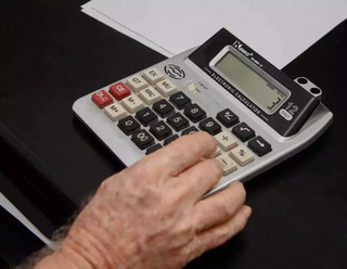 Homem utiliza calculadora para somar gastos mensais. (Foto: Alex Machado/Arquivo)