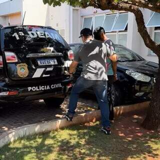 Suspeito sendo conduzido por policial civil na Deam, esta manhã (Foto: Divulgação)