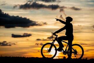 Imagem de um ciclista apontando para o céu, durante o pôr do sol (Foto: Divulgação)