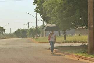 Mulher caminhando com sombrinha para se proteger do sol forte (Foto: Paulo Francis) 