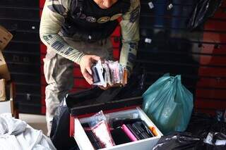 Policial guardando capinhas para celular apreendidas durante ação (Foto: PCMS/Divulgação)