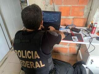 Policial federal vistoriando notebook em cumprimento a mandados. (Foto: Divulgação)