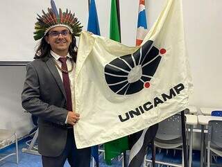 Um dos primeiros estudantes a se formar pelo vestibular indígena da Unicamp, Luiz Felipe Medina segura bandeira da instituição durante colação de grau (Foto: Arquivo pessoal)