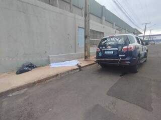 Corpo da vítima coberto por lençol ao lado da viatura da Polícia Militar (Foto: Alison Silva)