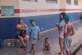 Márcia Rodrigues sentanda em cadeira da escola, com a vizinha Jéssica e três dos seus quatro filhos no corredor de alojamento improvisado (Foto: Marcos Maluf)