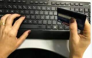 Mulher com cartão de crédito em frente ao computador. (Foto: Agência Brasil)