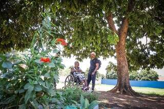 Matheus junto com a avó debaixo de árvore plantada no terreno (Foto: Henrique Kawaminami)