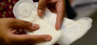 Mulher segura absorvente por dignidade menstrual (Foto: Agência Brasil)