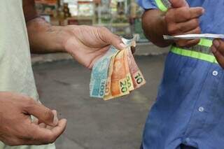 Homem repassando notas de R$ 100, R$ 50, R$ 20 e R$ 10 para outra pessoa, simulando uma forma de pagamento (Foto: Arquivo/Campo Grande News)
