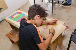 Criança pinta cartaz durante oficina artística (Foto: Arquivo/Campo Grande News)