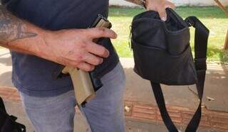 Policial. segura pistolas e bolsa com munições apreendidas na casa da vítima (Foto: Sidnei Bronka/Ligado na Notícia)