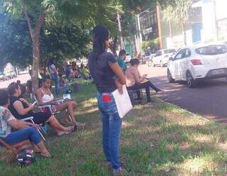 Pais e mães sentados no canteiro em frente à Defensoria esperando entrega das senhas (Foto: Direto das Ruas)
