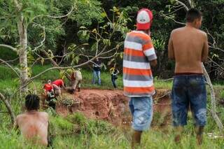 Bombeiros retirando corpo da vítima do lago e pessoas acompanhando de longe. (Foto: Henrique Kawaminami)