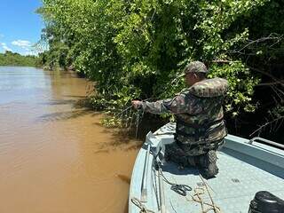 Policial militar ambiental retirando anzol de galho no rio Miranda (Foto: PMA)