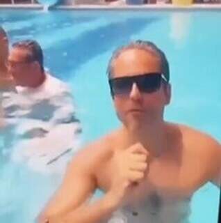 Nelson Cintra aparece em piscina de hotel, trajado com camiseta branca.