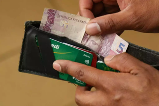 Em meio a carteira cheia de cartões, correntista segura cédula de R$ 5. (Foto: Arquivo/Alex Machado)