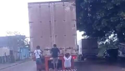 Crianças se penduram na traseira de caminhão em rua movimentada