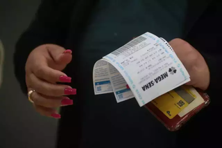 Apostadora segura carteira e comprovantes de aposta da Mega-Sena em agência lotérica de Campo Grande. (Foto: Arquivo/Marcos Maluf)