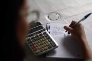 Mulher, que pode receber até 32,6% menos que homem em MS, faz lista de gastos do mês (Foto: Alex Machado)