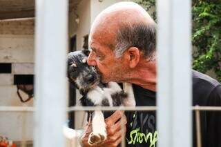 Maurício segura filhote no colo para dar carinho; ele faz parte dos 13 cães que o aposentado cuida (Foto: Henrique Kawaminami)