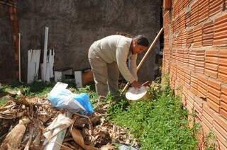 Agente comunitária da Prefeitura de Campo Grande realizando vistoria em terreno e retirando água acumulada em balde (Foto: PMCG)
