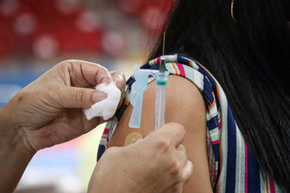 Profissional de saúde prepara curativo após aplicar vacina em mulher. (Foto: Arquivo/Campo Grande News)