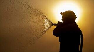 Combatente segura mangueira de água em contra-luz do sol (Foto: Joédson Alves/Agência Brasil)