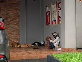 Roberto, morador de rua, debaixo de varanda com duas cachorras caramelo e o fiel companheiro de cor preta, na Avenida Bom Pastor (Foto: Natália Olliver)