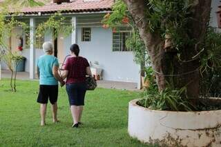 Idosa caminhando em um quintal com ajuda de mulher (Foto: Arquivo/Campo Grande News)