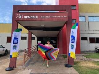 Gabrielly Antonietta, coordenadora do Centro Estadual de Cidadania LGBT, pousando com bandeira LGBT em frente ao Hemosul (Foto: Jéssica Fernandes)