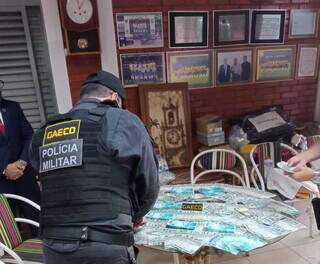 Na casa de Cezário, policial militar do Gaeco conta dinheiro apreendido e na parede, o &#34;passado&#34; do futebol em MS (Foto: Gaeco/Divulgação)