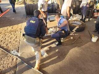 Policiais no momento em que retiravam tabletes de cocaína de pneus de caminhão (Foto: Divulgação)