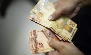 Pessoa com várias notas de R$ 50 e R$ 10 nas mãos (Foto: Marcello Casal Jr./ Agência Brasil)